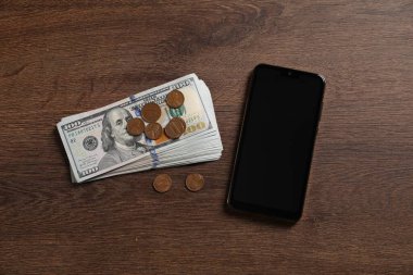 Akıllı telefon, dolar ve madeni paralar ahşap masada, düz yatıyordu.