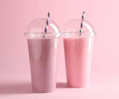 Pembe arka planda plastik bardaklarda lezzetli milkshake.