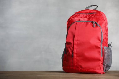 Gri arka planda, tahta masada kırmızı sırt çantası. Metin için boşluk