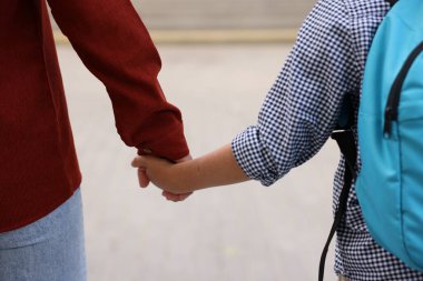 Anne oğluyla el ele tutuşup onu okula götürüyor.