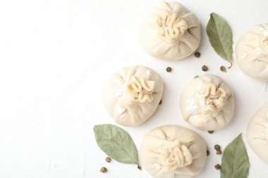 Beyaz masa üzerinde biber ve defne yapraklarıyla pişirilmemiş khinkaliler (hamur köfteleri). Metin için boşluk