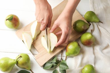 Beyaz ahşap masada taze olgun armut kesen bir kadın.