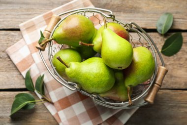 Metal sepetin içinde taze armutlar ve ahşap masanın üzerinde yeşil yapraklar.