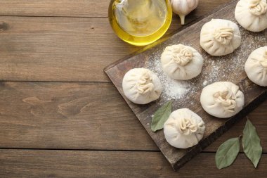 Tahta masa üzerinde un, sarımsak ve defne yapraklarıyla pişirilmemiş khinkaliler (hamur tatlısı). Metin için boşluk