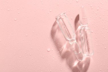 Pembe zemin üzerinde sıvı ve su damlaları olan cam ampuller. Metin için boşluk