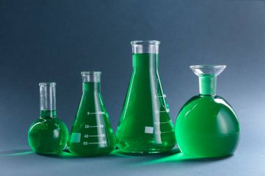 Gri zemin üzerinde yeşil sıvı bulunan laboratuvar camları.