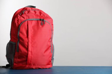 Kırmızı okul sırt çantası mavi ahşap masa üzerinde açık gri arkaplan, metin için boşluk