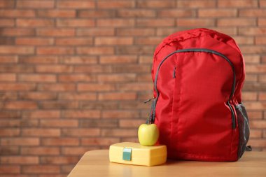 Sırt çantası, beslenme çantası ve elma kırmızı tuğla duvara karşı ahşap masada. Metin için boşluk