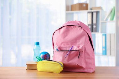 Sırt çantası, farklı kırtasiye malzemeleri, sınıfta masanın üstünde kitap ve bir şişe su.