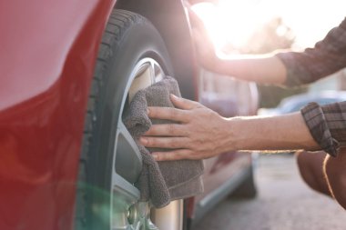 Dışarıdaki gri mikrofiber paçavralarla araba tekerleklerini silen adam, yakın plan.