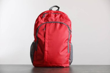 Gri masadaki kırmızı sırt çantası ışık arka planına karşı