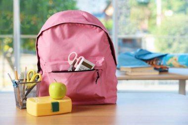 Sırt çantasında farklı kırtasiye malzemeleri, beslenme çantası ve elma var.