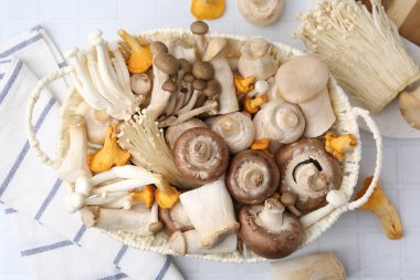Hasır sepetin içindeki farklı çiğ mantarlar beyaz döşemeli masada, düz yatıyordu.