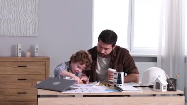 Meslek seçimi. Baba ve oğlu, masa içinde mühendislik çizimleri yapıyor, kamera içeri giriyor.