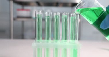 Bilim adamı laboratuardaki test tüpüne yeşil sıvı boşaltıyor.