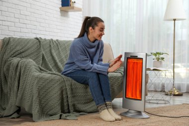 Evdeki elektrikli ısıtıcının yanında ellerini ısıtan kadın.