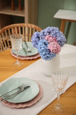 Yemek odasındaki ahşap masada, tabak ve vazo çiçekli şık bir ortam. İç tasarım