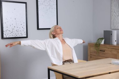 Gri duvarın yanındaki masada uzanan olgun bir kadın.