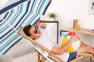 Güneş gözlüklü, plaj toplu mutlu adam evde güneşli yatakta eğleniyor. Denizde tatilin hayalini kuruyorum.