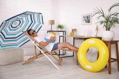 Güneş gözlüklü, plaj toplu mutlu adam evde güneşli yatakta eğleniyor. Denizde tatilin hayalini kuruyorum.