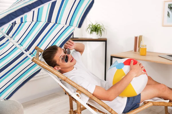 Güneş gözlüklü, plaj toplu mutlu adam evde güneşli yatakta eğleniyor. Denizde tatilin hayalini kuruyorum.