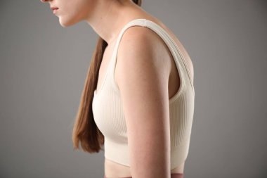 Gri arka planda kötü duruşu olan kadın, yakın plan.