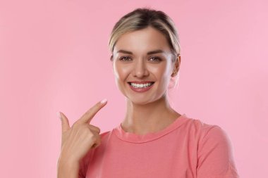 Pembe arka planda sağlıklı dişlerini gösteren bir kadın.