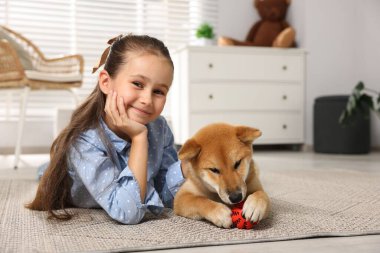 Evinde yerde köpeği ve evcil oyuncağıyla küçük şirin bir kızın portresi.