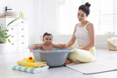 Anne küçük bebeğini evde yıkıyor.