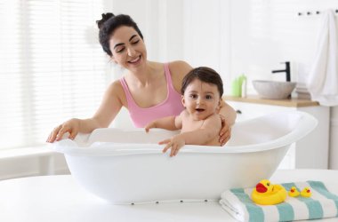 Anne küçük bebeğini evde yıkıyor.