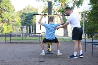 Spor aletleriyle egzersiz yapan genç bir adam profesyonel antrenörle dışarıda, arka planda. Metin için boşluk