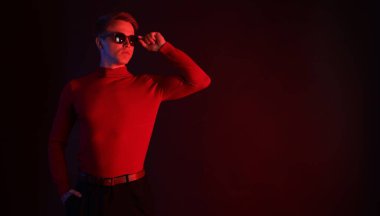 Güneş gözlüğü takan yakışıklı bir adam karanlık arka plana karşı neon ışıklar takıyor. Metin için boşluk