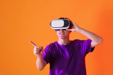 Sanal gerçeklik kulaklığı kullanarak gülümseyen adam ve turuncu arka planda bir şeye işaret eden neon ışıkları. Metin için boşluk