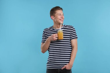 Açık mavi arka planda portakal suyu kavanozu olan mutlu bir adam. Tazeleyici içecek.