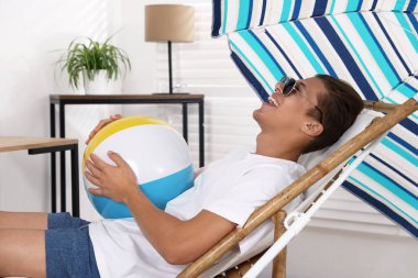 Güneş gözlüklü, plaj toplu mutlu adam evde güneşli yatakta eğleniyor. Denizde tatilin hayalini kuruyorum.