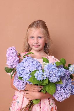 Bej arkaplanda bir buket Hortensiya çiçeğiyle güzel küçük bir kızın portresi.