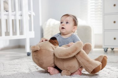 Küçük şirin bebek odada oyuncak ayıyla oynuyor.