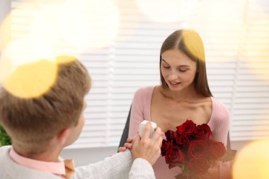 Nişan yüzüğü ve gül buketi olan bir adam mutlu kız arkadaşına evlenme teklif ediyor. Bokeh etkisi