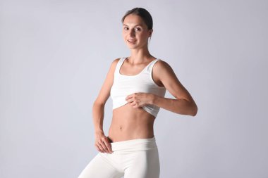 Açık gri arka planda düz göbekli bir kadın.