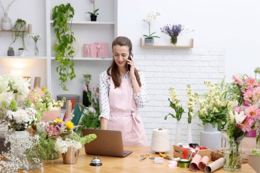 Profesyonel çiçekçi dükkanda çalışırken akıllı telefondan konuşuyor.