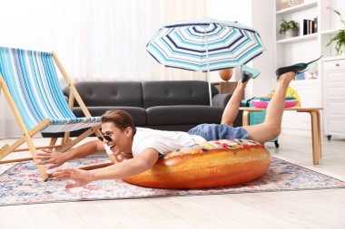 Güneş gözlüklü mutlu adam ve şişme yüzüklü paletler evde yerde eğleniyor. Denizde tatilin hayalini kuruyorum.