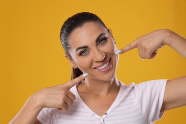 Sarı arka planda sağlıklı dişlerini gösteren bir kadın.