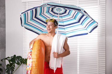 Evde şişme yüzüklü, dalış maskeli, havlulu ve plaj şemsiyeli mutlu adam var. Denizde tatilin hayalini kuruyorum.