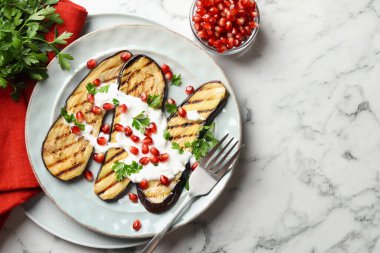 Nar tohumlu ızgara patlıcan dilimleri ve beyaz mermer masada yoğurt. Metin için boşluk