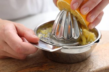 Meyve suyu. İçerideki masada meyve sıkacağı kullanan portakallı kadın, yakın plan.