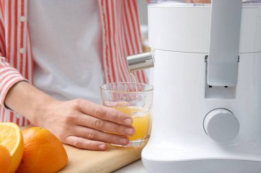 Kadın, modern meyve sıkacağıyla taze portakal suyu yapıyor.