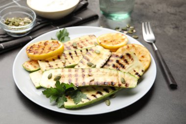 Lezzetli ızgara kabak dilimleri, balkabağı tohumları, limon ve maydanoz gri masada, yakın plan.