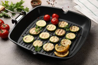 Lezzetli ızgara kabak dilimleri domatesli, limonlu ve maydanozlu tavada gri desenli masa, yakın plan.