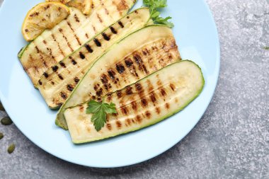 Lezzetli ızgara kabak dilimleri, maydanozlu ve limonlu gri desenli masa, düz.