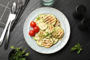 Lezzetli ızgara kabak dilimleri domatesli ve mikroyeşillikli siyah desenli masada servis ediliyor.